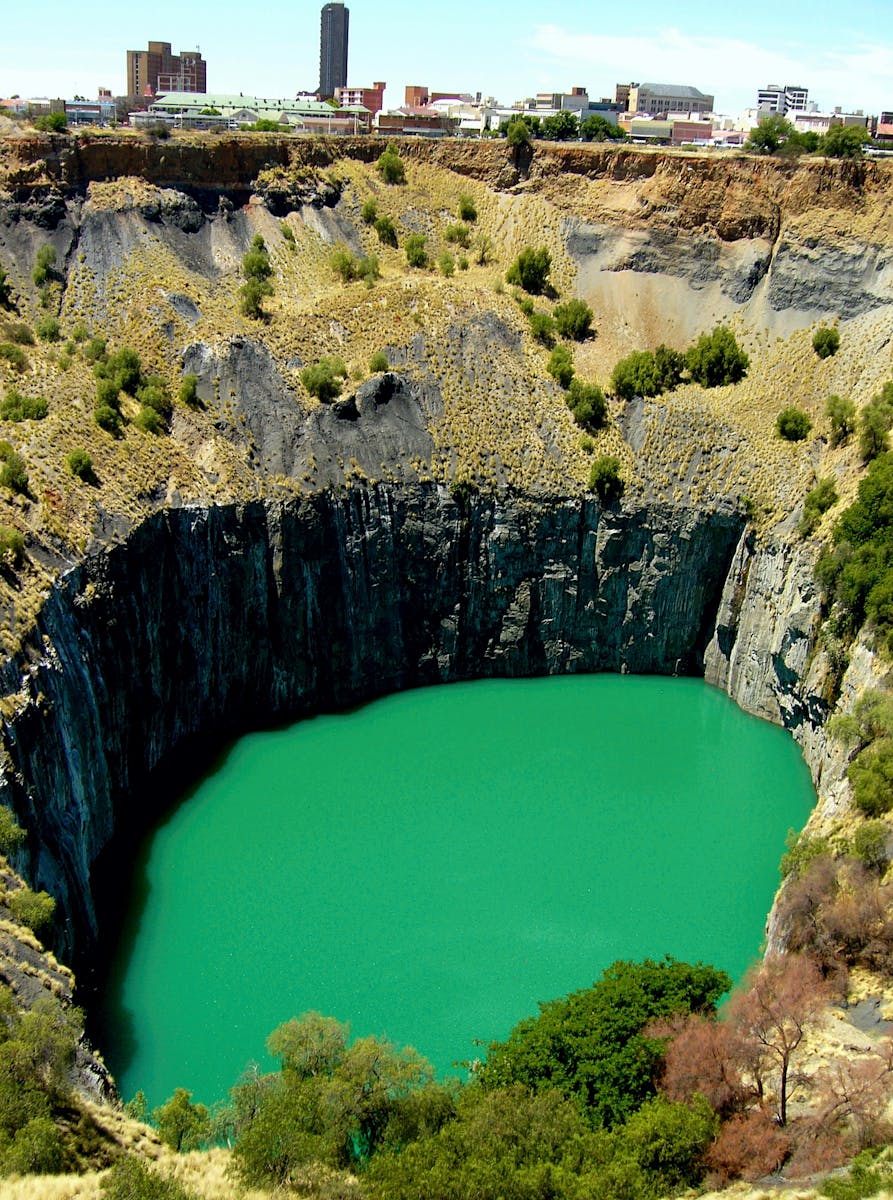 Explore the stunning Big Hole in Kimberley, South Africa, showcasing a deep, tranquil oasis surrounded by rugged cliffs.