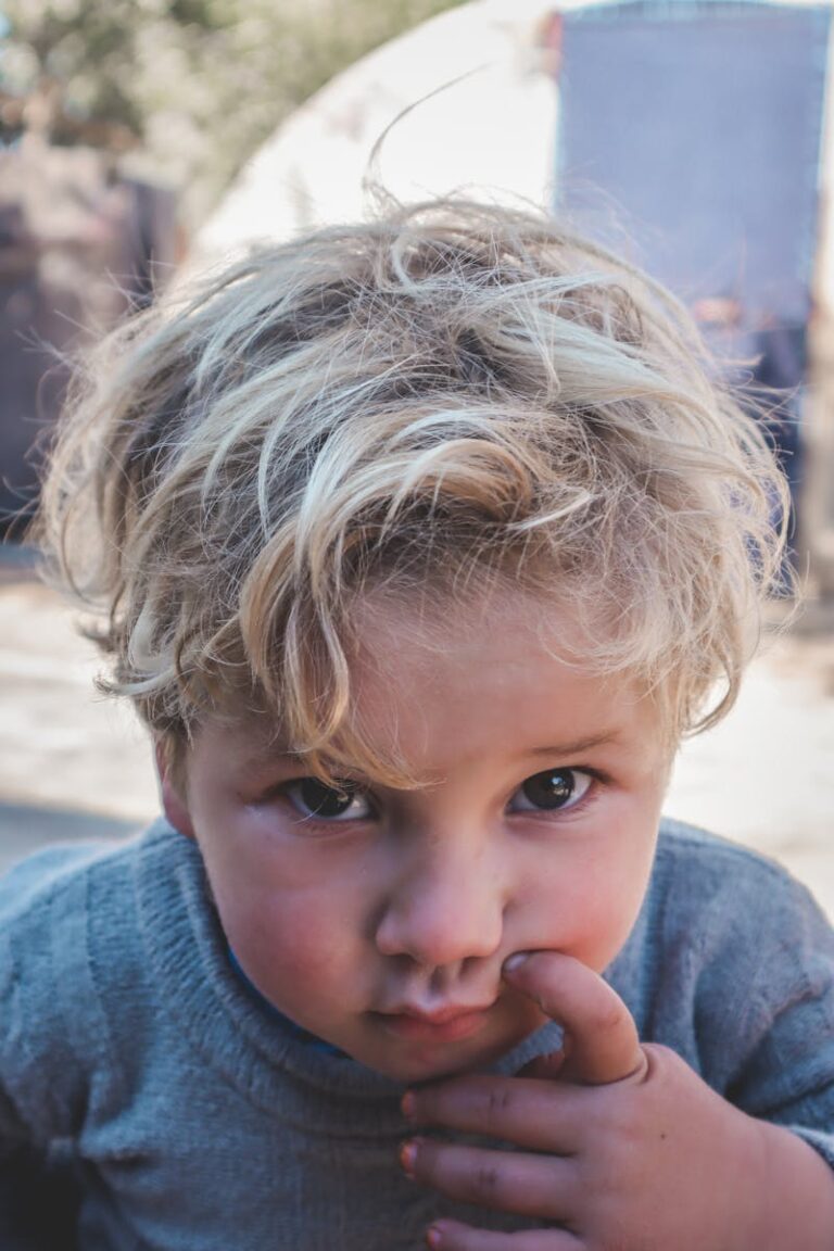 Close-up of a young child with blond hair, looking curious outdoors in Syria.