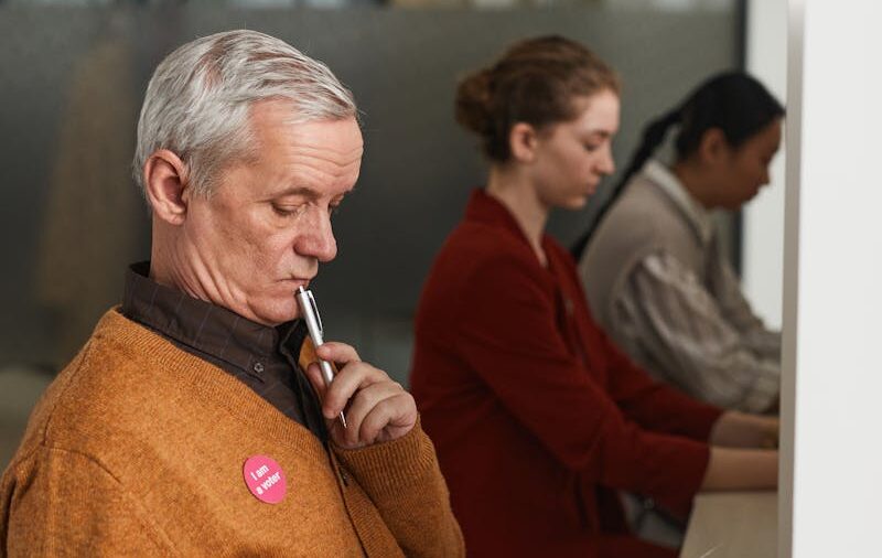 Senior man reviewing a ballot at an indoor polling station on voting day.