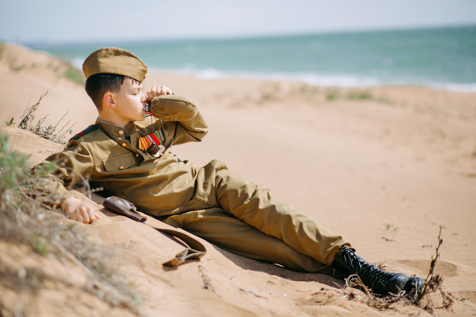 a boy in a military uniform sitting on a beach
