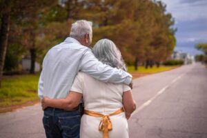 An older man and woman with grey hair walking arm in arm down a road